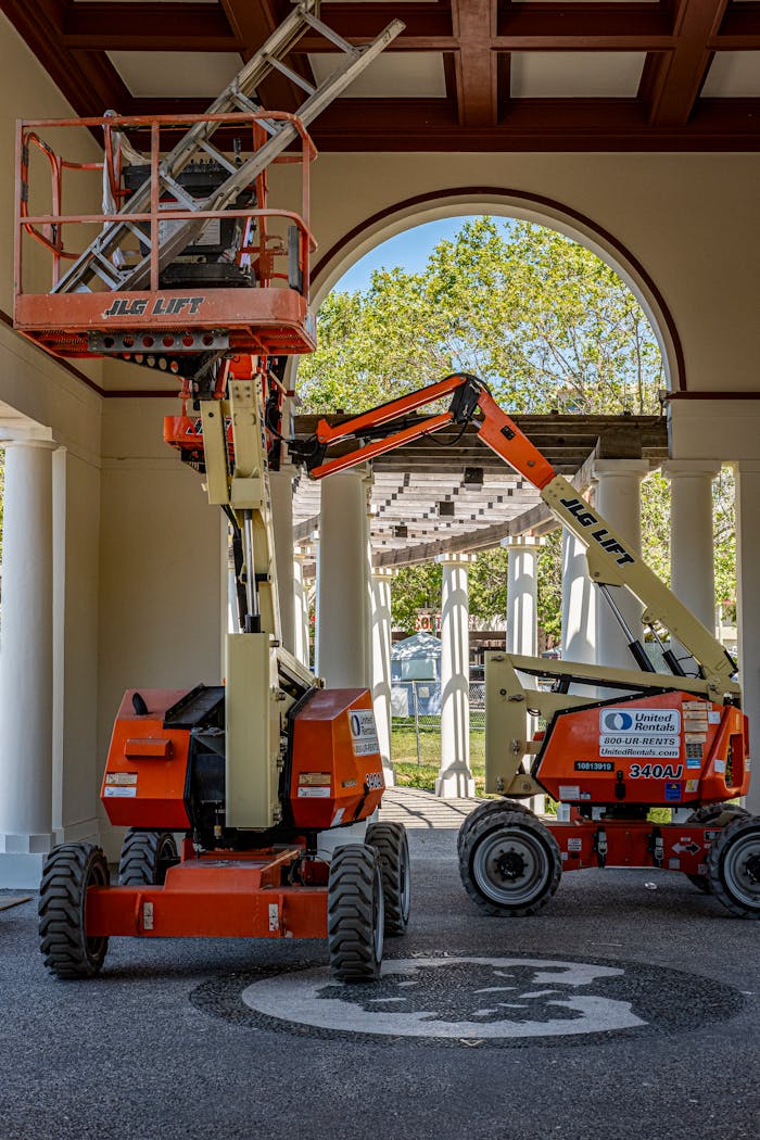 Two orange JLG lifts inside a building with a view outside through an archway.