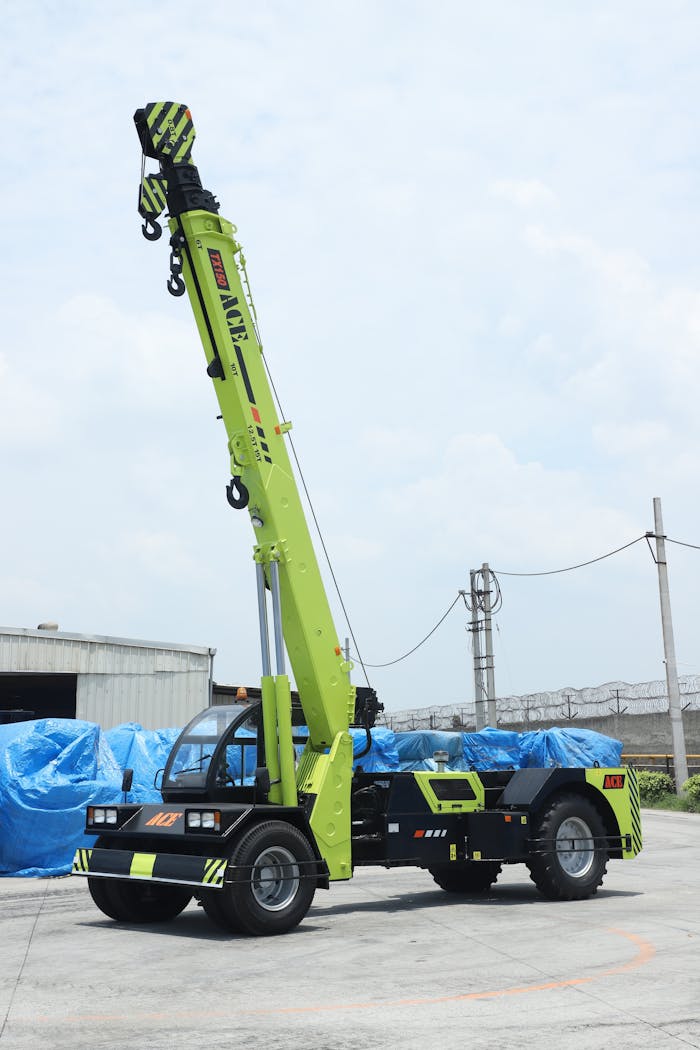 A vibrant ACE TX 150 crane stands ready in a Faridabad industrial yard under a bright sky.