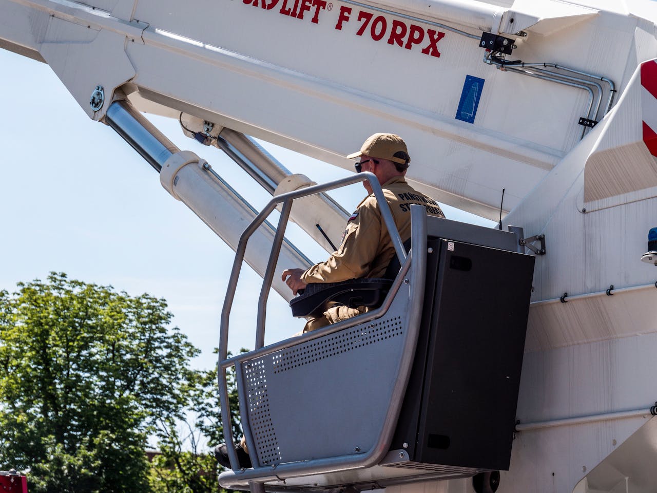Worker in uniform operating a high-reach lift outdoors on a sunny day.
